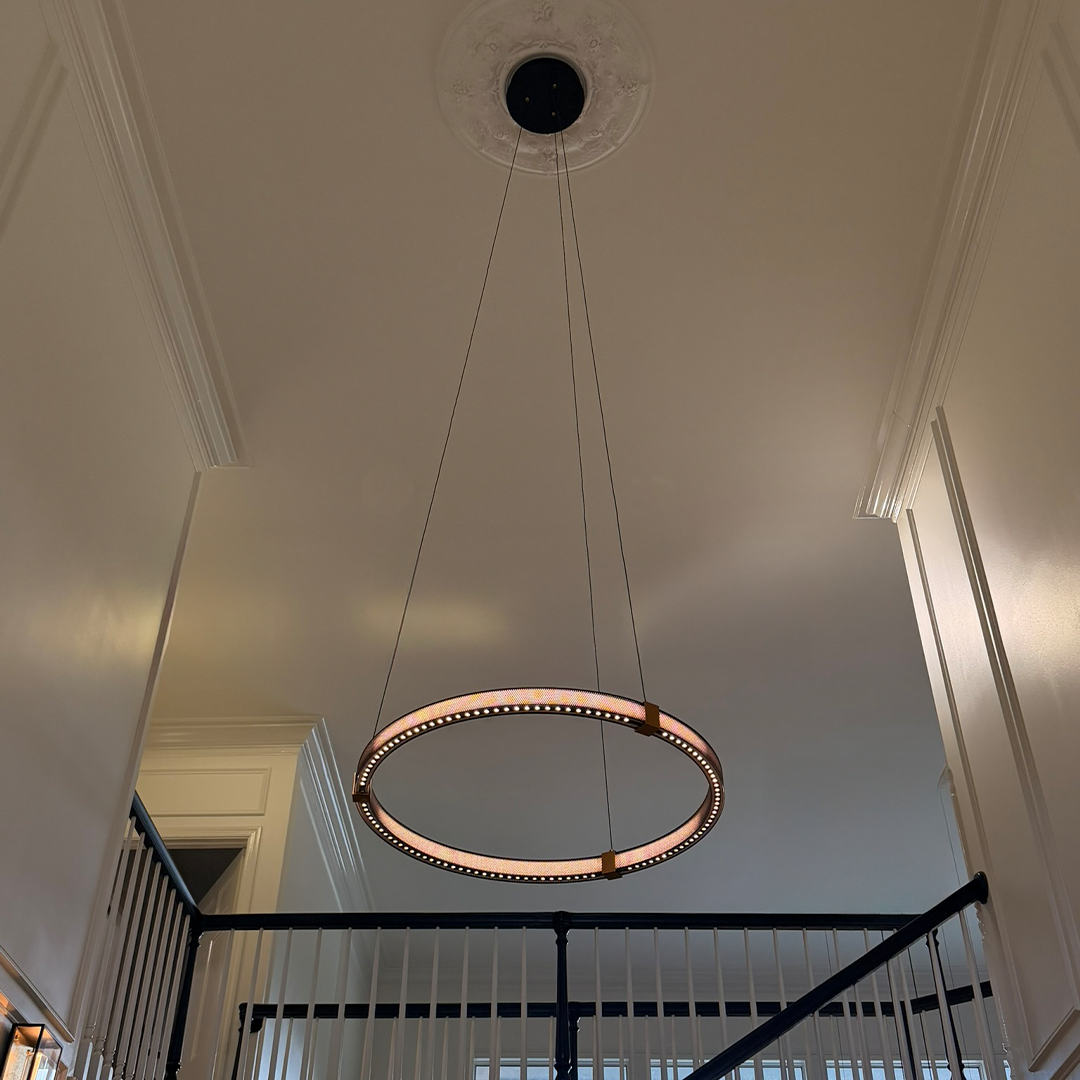 A single Matrix ring chandelier lit over a stairwell under a tall ceiling, Mistiva