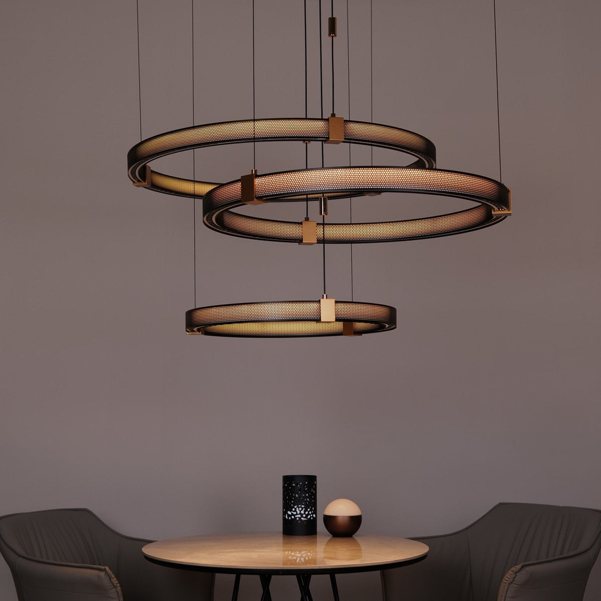 Three staggered Matrix ring chandeliers lit over a round dining table, Mistiva